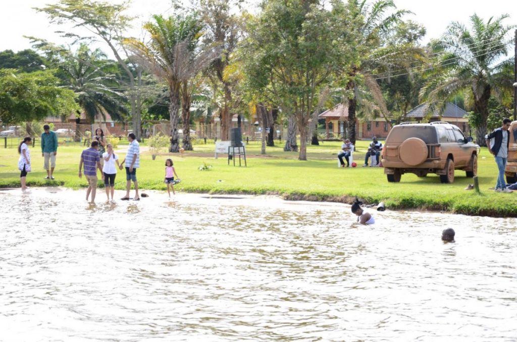 lake-nabugabo-detour | Uganda Car Rental Services People wading in a shallow pond at a sunny park while others stand nearby; a brown SUV is parked on the grass in the background with trees and houses beyond.
